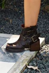 Botas cortas de cuero color marrón oscuro con hebillas y estribo desmontable.