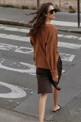 Camisa de lino color beige, con cuello solapa, escote en V y mangas largas. Presenta un diseño de bajo asimétrico con pliegues delanteros que generan un efecto abullonado.