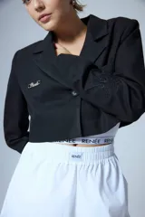 Saco sastrero corto a la cintura, color negro, con cierre frontal de un botón grabado, solapas clásicas, bolsillo ojal en el delantero, chapa metálica con logo en el pecho y bordado decorativo en la manga.