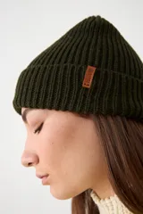Gorro tipo beanie de punto acanalado en color verde oscuro, con doblez en el borde y pequeña etiqueta de cuero sintético con logo.