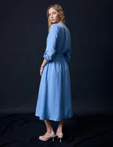 Vestido maxi color beige, con cuello mao y escote en V. Presenta mangas largas con presilla y botón para regular el largo, y un lazo ajustable en la cintura que marca la silueta.