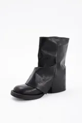 Botas de caña media confeccionadas en cuero vegano color negro, con diseño de solapa frontal y detalle de hebilla metálica en la parte superior.