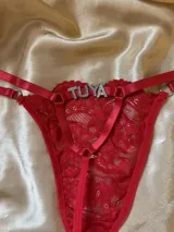 Tanga de hilo roja confeccionada en encaje, con tiras regulables y aplique de letras de strass con la palabra "TUYA".