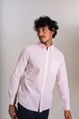 Camisa de manga larga confeccionada en tejido poplin con diseño de rayas verticales finas en color rosado y blanco. Presenta cuello abotonado (button-down), cierre frontal con botones y un bolsillo en el pecho.