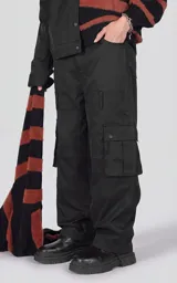 Pantalón cargo oversize de microfibra pesada en color negro, con silueta estructurada, bolsillos laterales de gran tamaño con solapa y broches snap, cintura elástica con cordón de ajuste y cierre frontal.