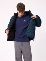 Campera reversible de nylon con cuello alto y cierre frontal. Un lado es de color gris liso con logo bordado, mientras que el otro lado presenta un estampado abstracto en tonos azules. Cuenta con bolsillos laterales y puños elásticos.