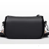 Cartera tipo baguette de color negro, confeccionada en eco cuero con textura granulada. Presenta un diseño compacto con cierre superior y una correa ajustable con detalles en tonos rojizos.