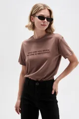 Remera de manga corta color marrón con cuello redondo y estampado frontal con la frase "Who are you when no one is watching?".