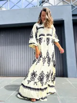 Vestido largo estilo túnica, color crudo con estampado en negro. Presenta cuello camisero con botones frontales, mangas anchas y corte amplio y fluido.