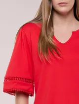 Remera blanca de silueta recta y algodón suave, con escote redondo y pequeña abertura central tipo gota. Presenta mangas de largo intermedio con aplicación horizontal de puntilla calada al tono y ruedo recto con tajos laterales.