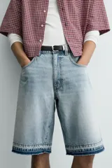 Bermuda de denim de algodón con efecto lavado desgastado en tonos marrones y azules. Tiene tiro medio, diseño de cinco bolsillos, pierna recta de corte holgado y bajo con acabado irregular. Cuenta con cierre frontal de cremallera y botón metálico.