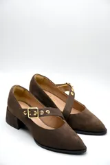 Zapato tipo Mary Jane de gamuza color marrón, con taco cuadrado medio y tira ajustable en el empeine con hebilla metálica dorada y detalles de ojalillos.