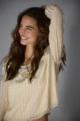 Camisa de manga larga en color crema, con diseño bordado en hilos dorados y plateados que forman líneas verticales y detalles florales en el pecho. Presenta un estilo elegante y sofisticado con aplicaciones brillantes.