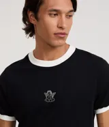 Remera de manga corta color negro, de corte ajustado tipo baby tee, con cuello redondo y puños en color blanco. Presenta un pequeño bordado de un ángel en el centro del pecho.
