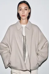 Chaqueta de lana en color beige, con cuello solapa, cierre frontal con cremallera metálica, mangas largas con corte evasé y bajo asimétrico.