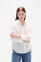 Camisa de algodón blanca, de corte clásico con cuello camisero, cierre frontal con botones, mangas largas con puños y bolsillo frontal en el pecho.