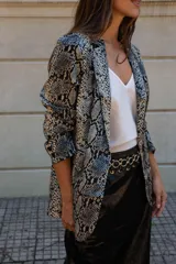 Blazer de corte sastrero con estampado de piel de serpiente en tonos grises y negros. Presenta solapas clásicas, cierre frontal con botones y mangas largas con detalle de botones en los puños.