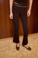 Pantalon negro de corte flare, confeccionado en tejido elastizado. Presenta tiro alto, cintura elastizada y detalle de tachas metálicas decorativas en la parte superior.