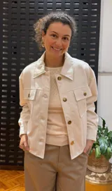 Campera color crema de algodón forrada, con cuello camisero, cierre frontal con botones a tono, bolsillos con solapa abotonada en el pecho y corte holgado.