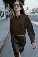Camisa corta de cuello solapa y manga larga, con trabillas decorativas en los hombros. Presenta pliegues delanteros, elástico en la espalda y cierre frontal con botones.