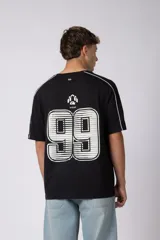 Remera de algodón color blanco con corte regular, cuello redondo y mangas cortas. Presenta detalles de líneas finas negras en los hombros y estampado gráfico frontal con tipografía y logotipos en color negro.