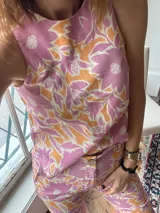 Top sin mangas con cuello redondo, confeccionado en lino con estampado floral en tonos rosados y naranjas. Presenta un diseño con cierre de tres lazos en la espalda.