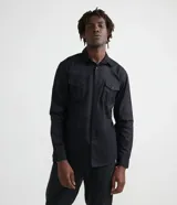 Camisa de manga larga color negro, confeccionada en sarga de algodón. Presenta cuello clásico, cierre frontal de botones y dos bolsillos de parche con solapa y botón en el pecho.