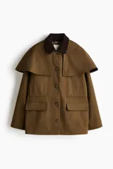 Chaqueta de sarga color marrón con cuello de pana de algodón oscura, capa decorativa desmontable, cierre de botones delanteros, bolsillos con solapa y cordón interior para ajustar la cintura.
