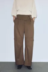 Pantalón cargo de tiro medio en color marrón, confeccionado con mezcla de lana. Presenta cintura con detalle de vuelta, pliegues frontales, bolsillos laterales y bolsillos con solapa en las piernas. Cierre frontal con cremallera, botón y ganchos metálicos.