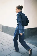 Jeans de tiro alto, pierna ancha y corte recto, confeccionado en denim de algodón rígido de color azul medio. Presenta un detalle de herrajes metálicos en la cintura.