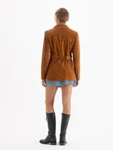 Parka de gamuza color ocre con diseño de estilo safari, cuello camisero, cierre frontal con broches metálicos, múltiples bolsillos frontales y cinturón ajustable con hebilla metálica.