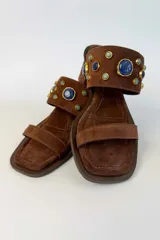 Sandalia de tacón ancho color marrón, confeccionada en gamuza, con puntera cuadrada, tira delantera fina y tira ancha superior decorada con apliques de piedras en tonos azules y bordes dorados.