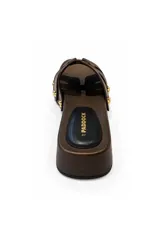 Sandalia tipo zueco Paddock de color negro, con plataforma baja de aspecto amaderado y tiras entrelazadas en el empeine. Presenta detalles de tachas metálicas doradas en los laterales y plantilla acolchada.