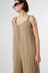 Mono largo de muselina de algodón color beige, con escote en V, tirantes ajustables mediante lazos para atar en los hombros y diseño amplio de corte holgado.