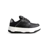 Championes deportivos Via Marte modelo Kalea, de color negro con textura combinada en cuero sintético liso y granulado. Presenta una suela de plataforma blanca con detalle de logo grabado y un aplique decorativo en los cordones.