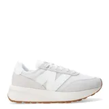 Championes urbanos New Balance modelo 370, de diseño retro inspirado en los años 70. Presentan una combinación de tonos blancos y gris claro, con paneles de malla y superposiciones de gamuza. Incluyen el logo N en los laterales, cierre con cordones y una suela de goma con plataforma y base color caramelo.