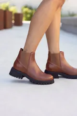 Botas Chelsea de cuero color marrón, estilo botín corto, con elástico lateral y detalle de textura de cocodrilo en el talón. Cuentan con suela track negra gruesa y baja.