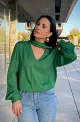 Blusa de satén color verde, con cuello en V y detalle de lazo integrado al cuello. Presenta mangas largas abullonadas con puños ajustados.