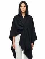 Ruana de tejido soft color negro, con cuello en V y un nudo o pasador frontal que ajusta la prenda. Los bordes tienen terminación desflecada.