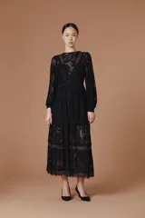 Vestido largo de encaje color blanco, con mangas largas abullonadas, cuello redondo y falda con volados en el ruedo. Presenta un diseño con transparencias y forro interno.