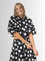 Conjunto de dos piezas con estampa polka dots en negro y blanco, compuesto por un pantalón tipo culotte de tiro alto con bolsillos y una blusa estilo camisa con mangas globo y cierre frontal de botones.