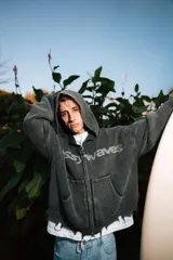 Campera de punto gris oscuro con capucha, cierre frontal completo y bolsillos delanteros tipo canguro. Presenta diseño texturizado en canalé grueso, detalles desgastados en los bordes y el texto "ssy waves" bordado en el pecho.