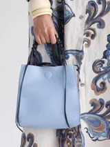 Cartera celeste de cuero con asa corta trenzada color negro y tiras colgantes decorativas.