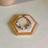 Pulsera elástica con cuentas de cerámica blanca con diseño floral azul, separadores de cristal facetado color bronce y cadena de eslabones dorada.