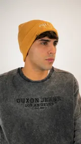 Gorro tipo beanie de punto acanalado color mostaza con bordado frontal en hilo de color claro.