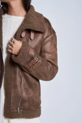 Campera gamulán marrón de símil cuero, con interior de corderoy al tono, cierre frontal con cremallera y cuello con solapas grandes. Presenta detalles de hebillas en los puños y bolsillos laterales con cierre.