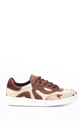 Championes de cuero con diseño de paneles orgánicos en tonos tierra. Presenta una combinación de cuero liso marrón y beige, con detalle de cuero con pelo estampado tipo vaca en la puntera. Cuenta con cordones al tono y suela blanca.