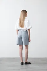 Bermuda de denim azul claro con rayas verticales blancas, de corte relajado y largo hasta la rodilla. Presenta pespuntes a contratono.