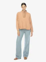 Sobrecamisa de algodón color salmón claro con cuello alto y cierre parcial de botones. Presenta mangas ranglan y textura sutilmente arrugada o plisada.