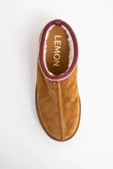 Zueco de gamuza color camel con interior forrado en piel sintética. Presenta una guarda bordada decorativa en el borde superior y una suela de plataforma de goma color marrón.